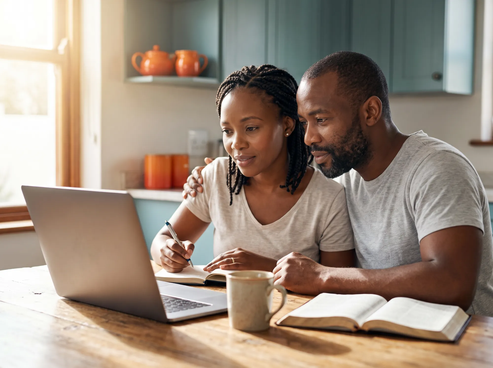 Husband and wife at their kitchen table joining an online pastoral counseling session on a laptop, with an open Bible and notebook