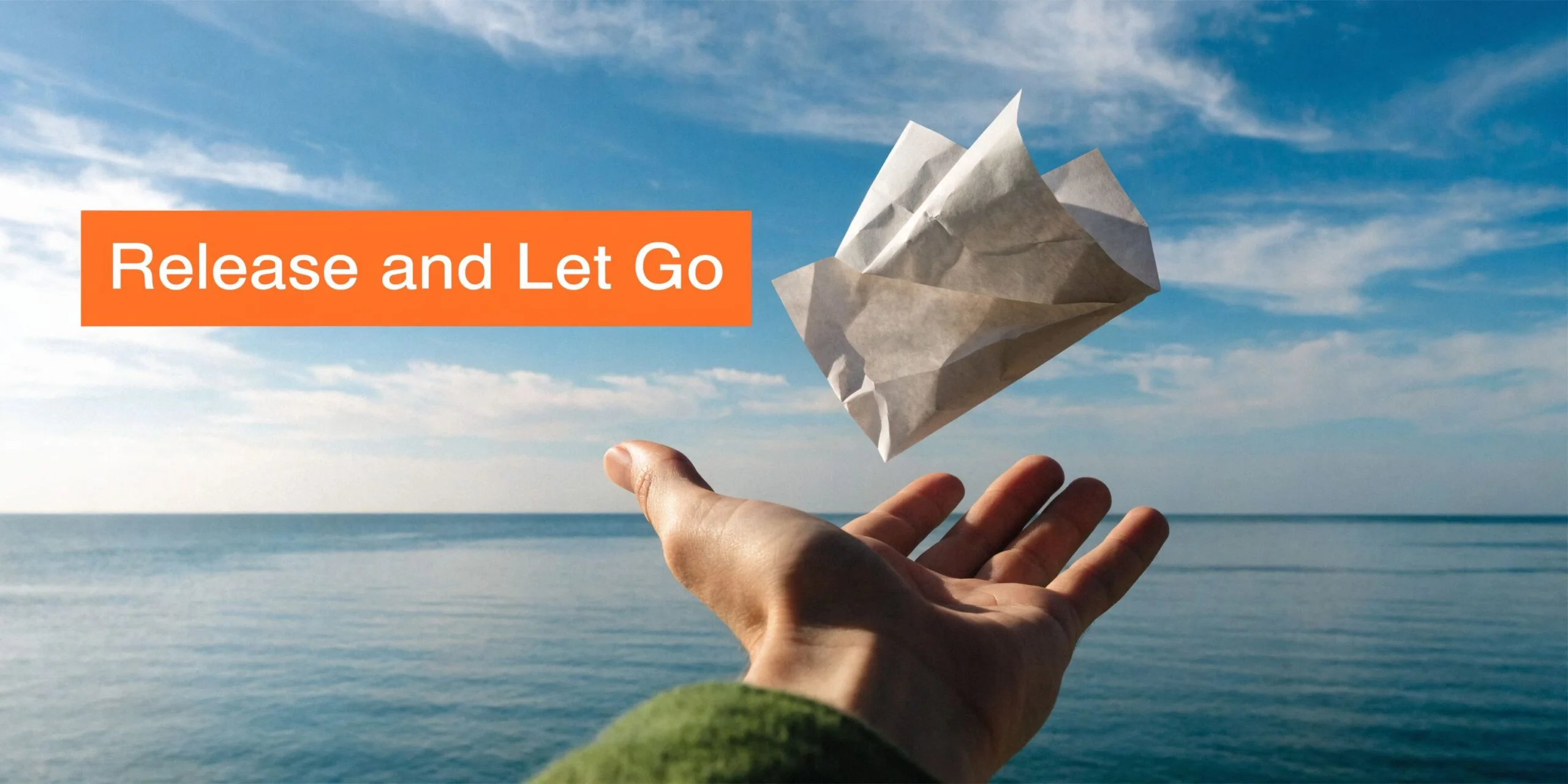 A hand releasing a crumpled piece of paper into the air above a calm sea.